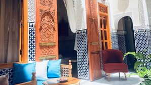 Um interior tradicional marroquino com portas elaboradas, um sofá, uma cadeira vermelha e um chão estampado.