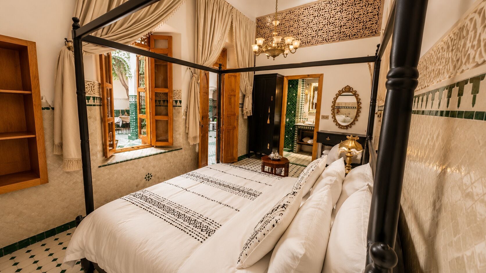 A four-poster bed with a patterned bedspread, a chandelier, and a mirror on the wall.