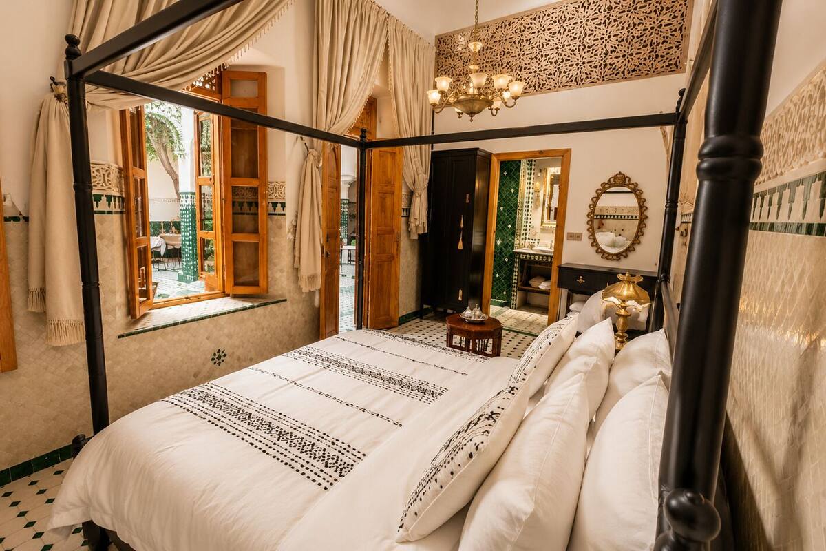 A four-poster bed with a patterned bedspread, a chandelier, and a mirror on the wall.