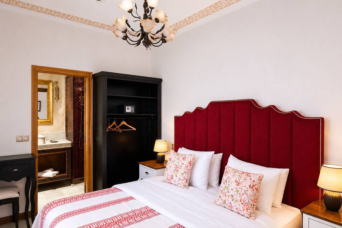 A hotel room with a bed, bedside table, nightstand, wardrobe, desk, and a chandelier.