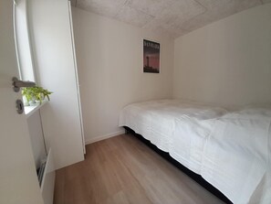 A bedroom with a bed, a window with a plant, and a poster on the wall. - Holiday home in the forest close to water (Hadsund)