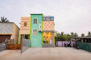 Un immeuble à plusieurs étages, doté d’une façade verte et beige, avec une enseigne indiquant que des chambres sont disponibles, et une moto garée à l’extérieur.