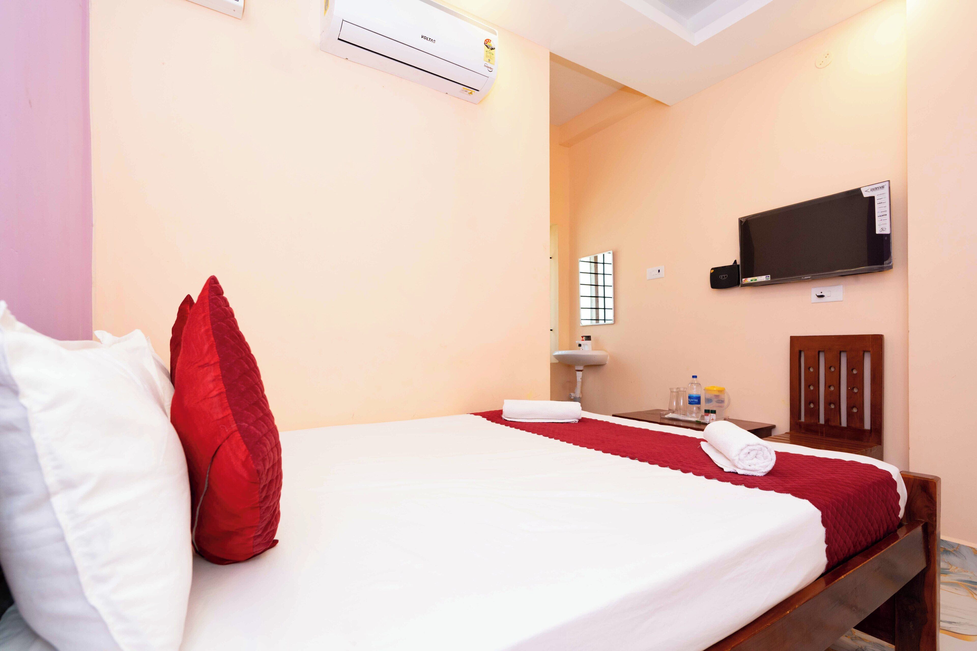 Una habitación de hotel con cama, televisor montado en la pared, lavamanos y espejo.