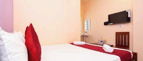 Una habitación de hotel con cama, televisor montado en la pared, lavamanos y espejo.