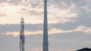 Une tour de télécommunications et un bâtiment doté d’un toit en forme de flèche, se dressant sur un ciel nuageux.