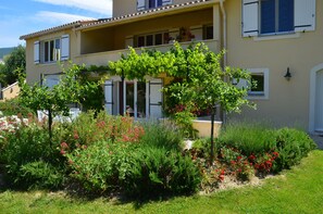 En toetagers bygning med balkon, omgivet af en have med forskellige planter og blomster.