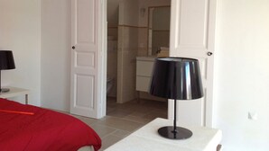 Una habitación de hotel con cama, mesita de noche, lámpara y puerta que da a un baño.