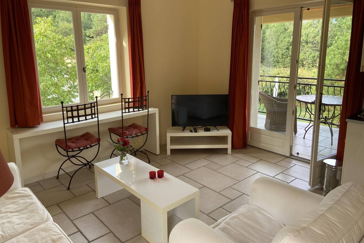 Un salón con televisor, sofá blanco y una mesa con vasos rojos.