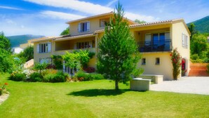 Una casa de dos pisos con balcón, rodeada de un jardín cuidado y un cielo despejado.