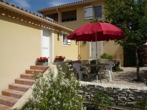 A yellow building with a red umbrella, white chairs, and a stone wall. - VillaFleuryAppartement (Montbrun-les-Bains)