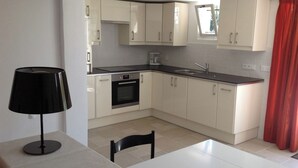Una cocina moderna con armarios blancos, encimera negra, horno integrado y ventana con cortina roja.