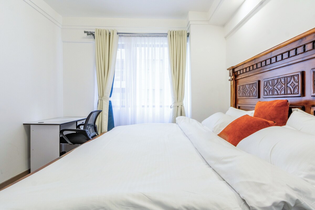 A hotel room with a bed, desk, chair, and curtains.