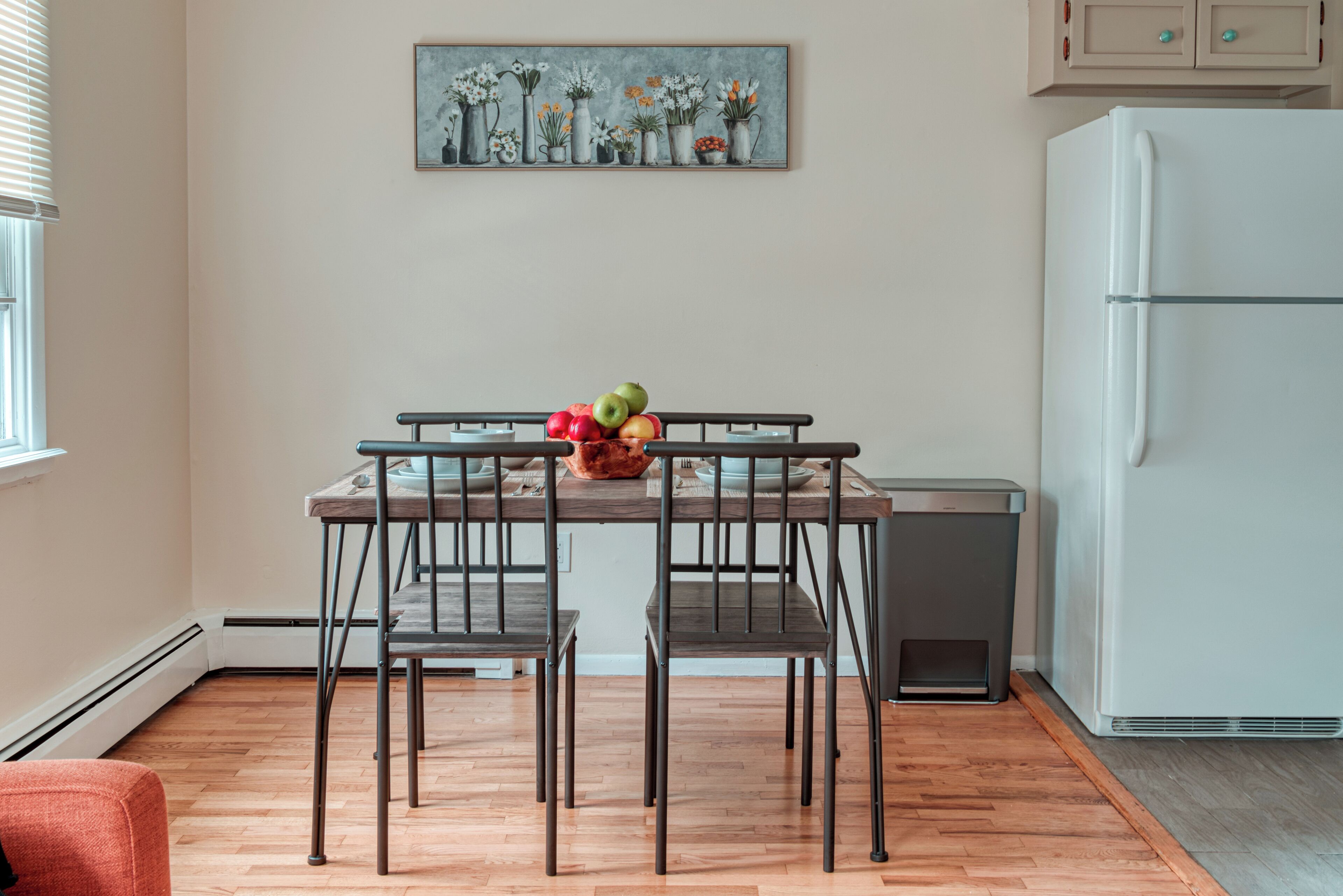 A kitchen with a dining table, chairs, a refrigerator, and a fruit bowl.