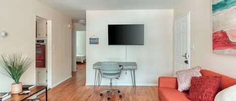 A living room with a TV mounted on the wall, a grey office chair, a red sofa, and a striped rug.