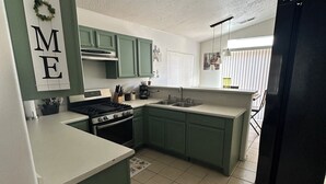 A modern kitchen with green cabinets, a large island, and a 'HOME' sign on the wall.