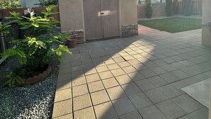 A small building with a wooden door, surrounded by a paved patio and gravel.