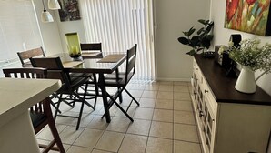 A dining area with a table and chairs, a ceiling light fixture, a window with blinds, and a painting on the wall.