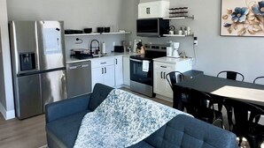 A modern kitchen with stainless steel appliances, a dining area with a table and chairs, and a sofa with a patterned throw.