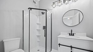 A modern bathroom with a glass-enclosed shower, a white toilet, and a vanity with a mirror.