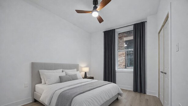 A bedroom with a bed, a nightstand, a ceiling fan, a window with curtains, and a door.