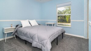 Une chambre à coucher comprenant un lit, une table de chevet, une fenêtre donnant sur un paysage verdoyant et un ventilateur de plafond.