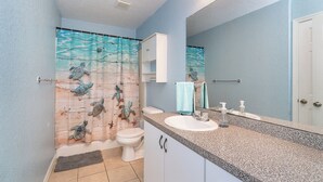 Une salle de bain avec un rideau de douche orné de motifs de tortues de mer, un lavabo blanc et un miroir au-dessus.