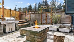 An outdoor patio with a stone fire pit, a grill, and planters.