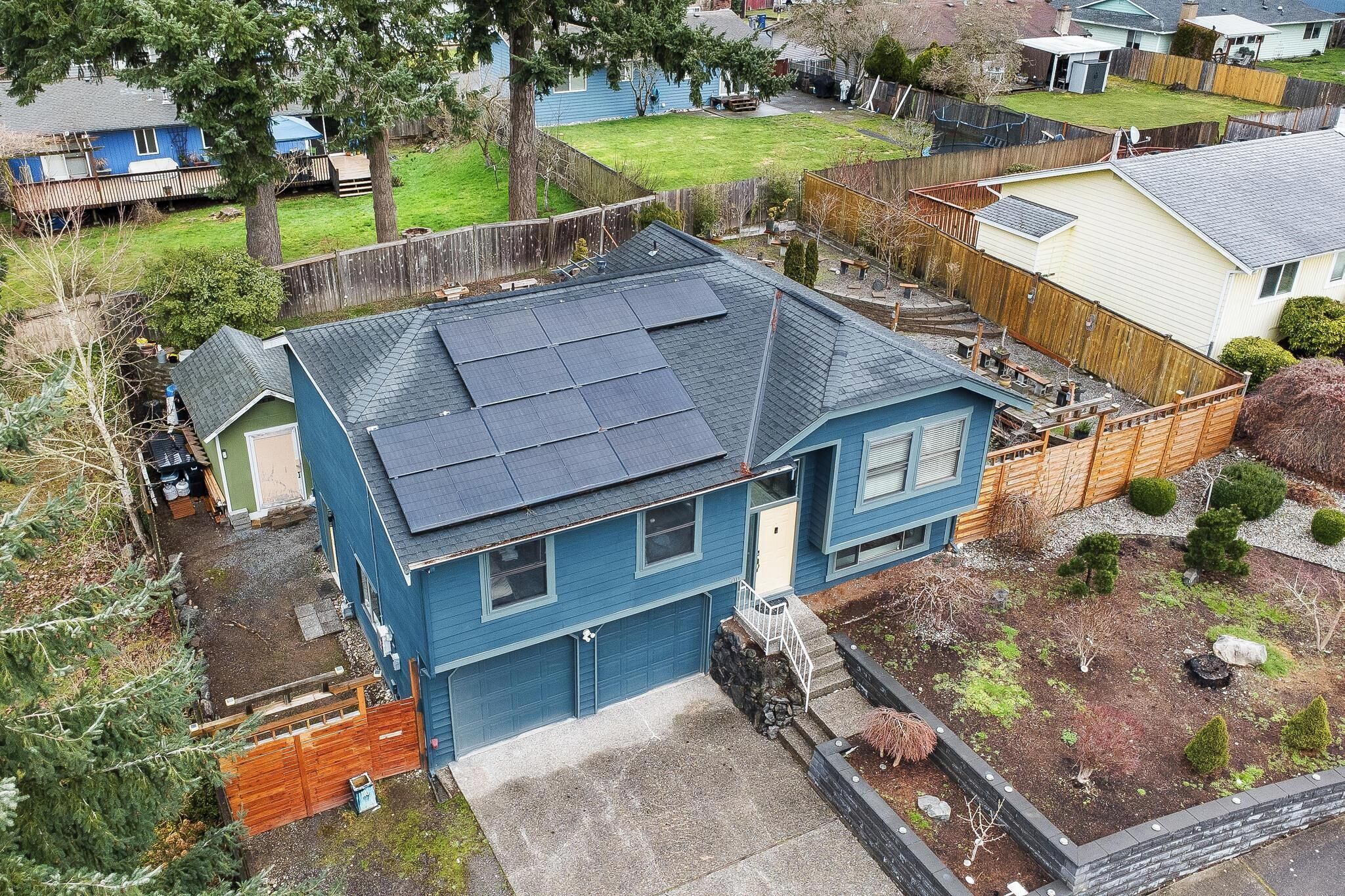 Una casa de dos pisos con fachada azul, techo inclinado y un jardín pequeño con cerca de madera en el frente.