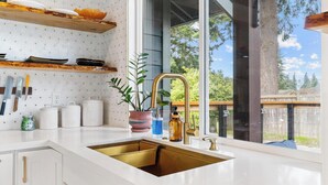 A modern kitchen with a large window, white cabinetry, and a gold sink.