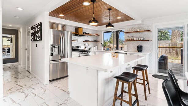 A modern kitchen with a large island, stainless steel appliances, wooden ceiling, and a view to the backyard.