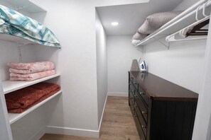 A compact storage area with shelves for folded towels, a wooden dresser, and a hanging rack for clothes. - The Magnolia Retreat 4Bed/3Bath Luxury Retreat | Heated Pool | Near Beach & Port (Cape Canaveral)