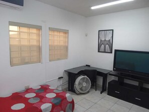 Une chambre avec un lit, un bureau, une chaise, une télévision et un ventilateur.