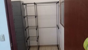 Ett rum med en hyllsektion i metall mot en vit vägg, en dörrkarm i trä och ett klinkergolv.