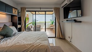 Ein Schlafzimmer mit einem großen Bett, einem an der Wand montierten Fernseher und einer Glastür, die auf eine möblierte Terrasse im Freien führt.