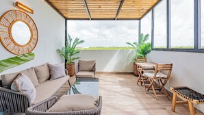 Ein modernes Wohnzimmer mit Holzboden, großen Fenstern, einer Couch, einem Couchtisch und zwei Zimmerpflanzen.