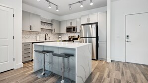 A modern kitchen with white cabinets, a marble island with bar stools, stainless steel appliances, and a wooden floor. - Pure Suites 2 Bed Downtown Phoenix Pool Gym (Phoenix)