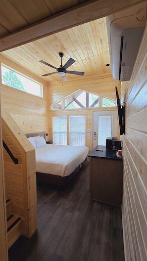 Una cabaña de madera con una cama, un escritorio y un ventilador de techo.