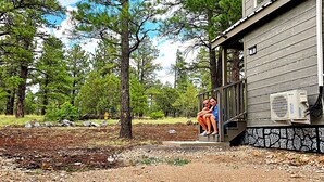 Una cabaña con cimientos de piedra y una terraza de madera, rodeada de árboles.