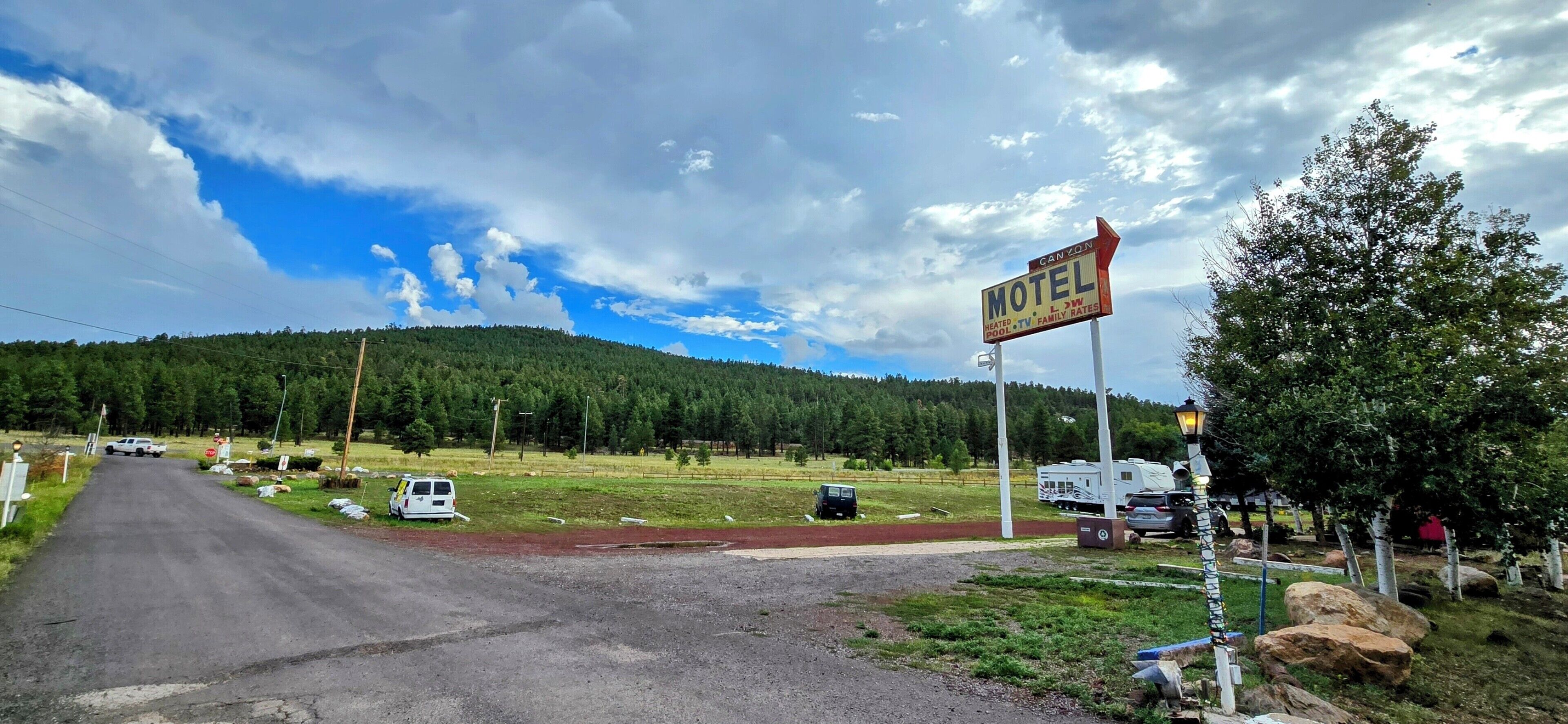 Placa de motel com montanhas ao fundo, estrada de terra e veículos estacionados.