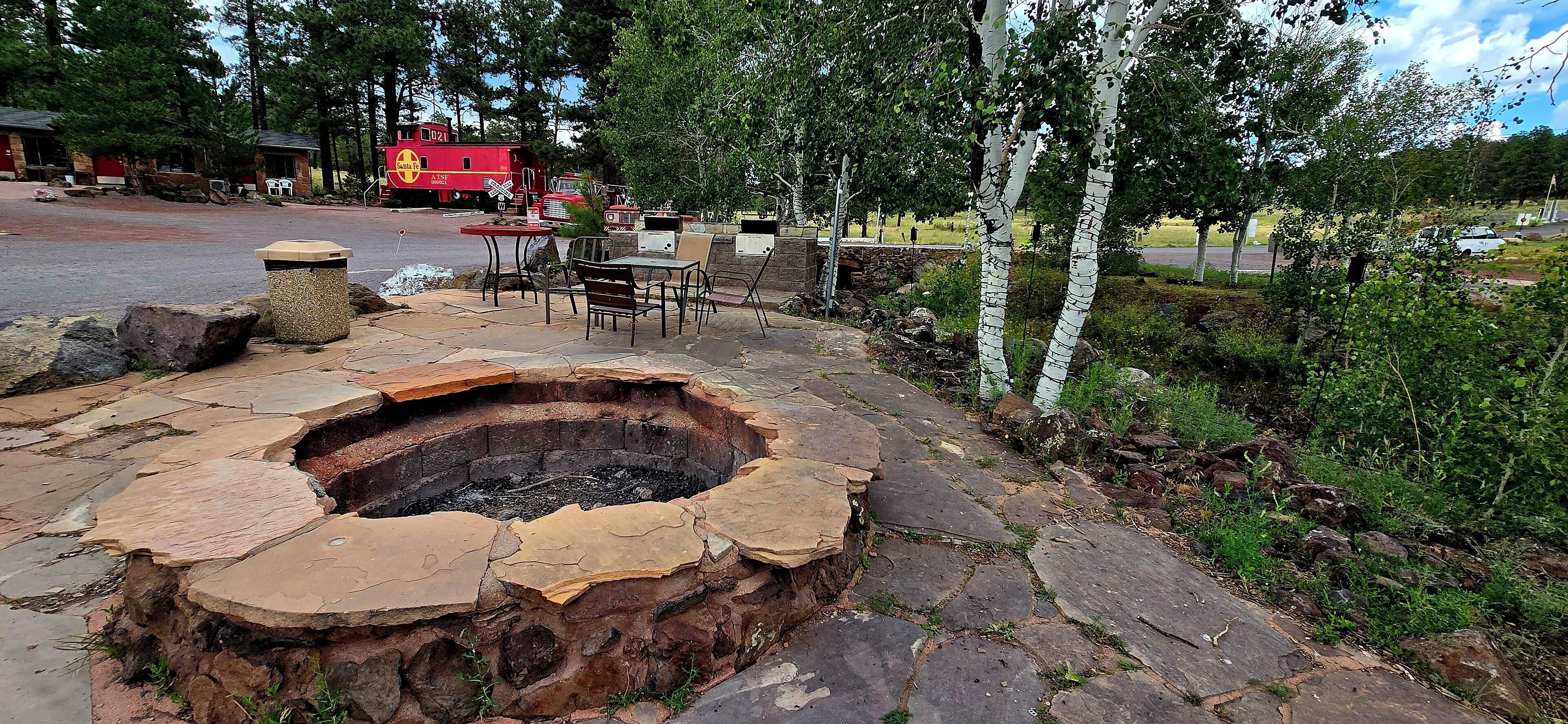 A stone fire pit with outdoor seating, surrounded by birch trees and a stone pathway.