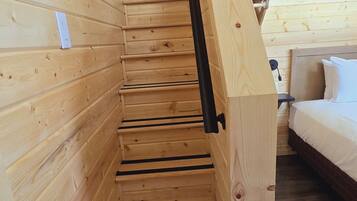 Een houten trap met een zwarte leuning die leidt naar een slaapkamer met een bed en een nachtkastje.