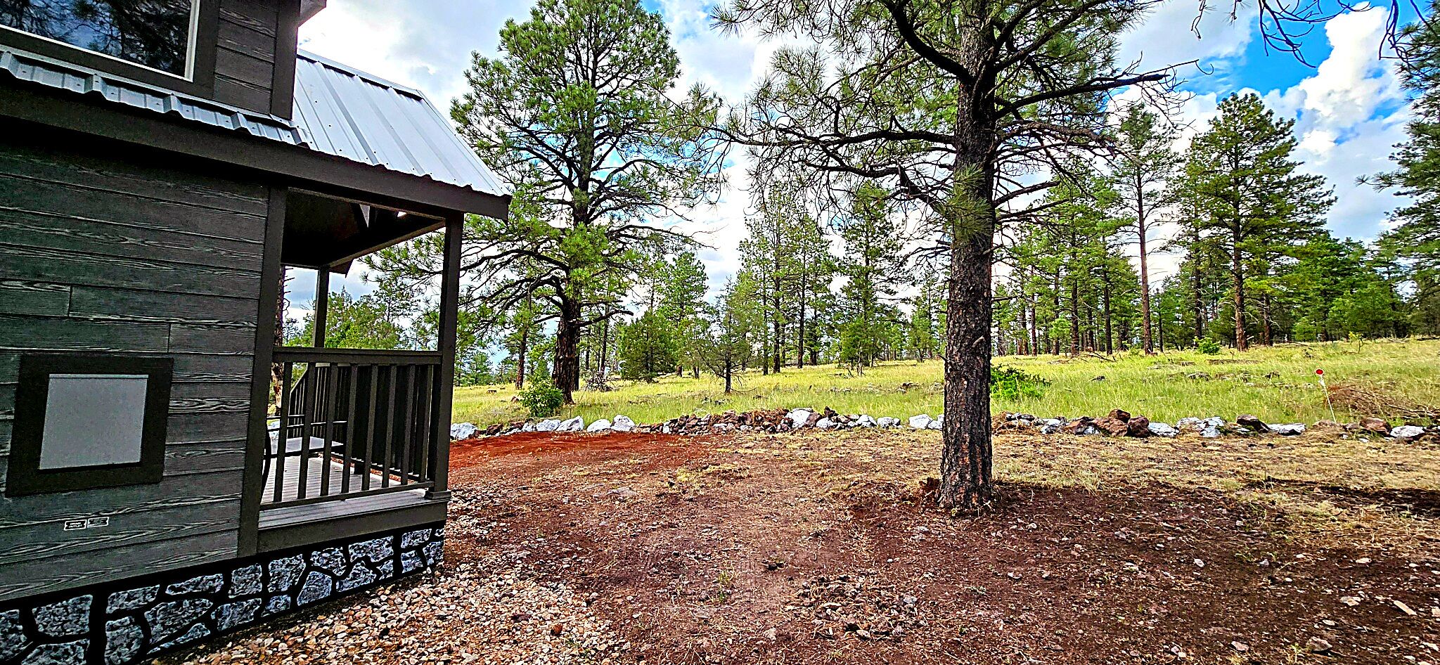 A cabin with a wooden exterior, a porch, and a view of a forested hillside.