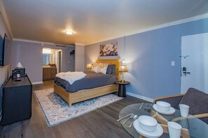A modern bedroom with a bed, bedside lamps, a small table with plates and cutlery, and a TV on a stand. - Mins to Hospitals*Arenas*Stadiums*Uptown & Museums (Charlotte)