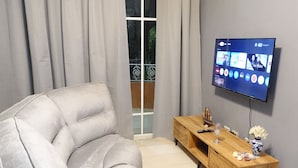 Uma sala de estar moderna com um sofá cinzento, um móvel de televisão de madeira e uma televisão de ecrã plano fixada na parede.