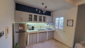 Uma cozinha compacta com armários brancos, geladeira de aço inoxidável, fogão a gás e uma janela com vitrais.