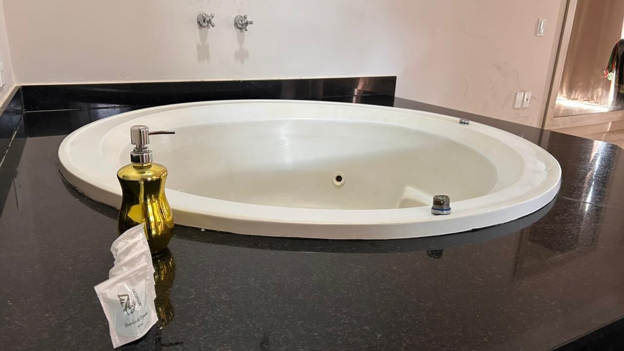 Een badkamer met een witte, ovale wasbak, een fles handzeep en een klein pak zakdoekjes op een zwart aanrecht.