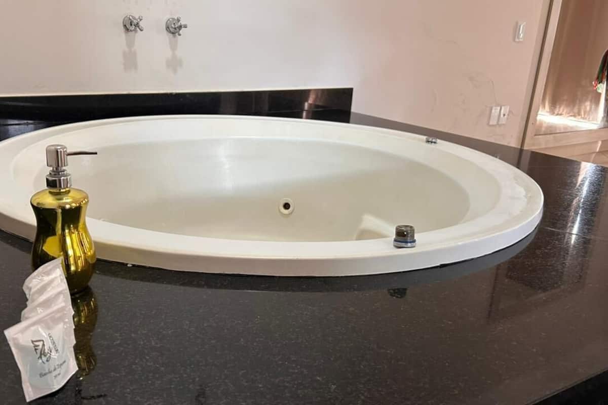 Een badkamer met een witte, ovale wasbak, een fles handzeep en een klein pak zakdoekjes op een zwart aanrecht.
