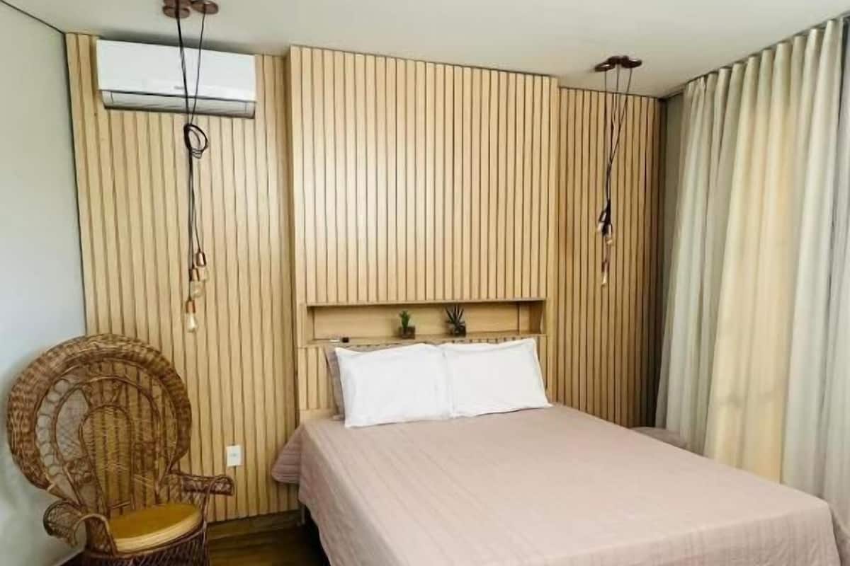 Een slaapkamer met een bed, een rieten stoel, houten paneelwanden en een plafondventilator.