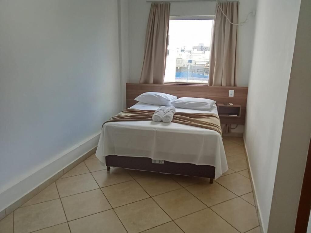 A small, neatly made bed with white bedding and a towel, a wooden headboard, and a window with curtains.