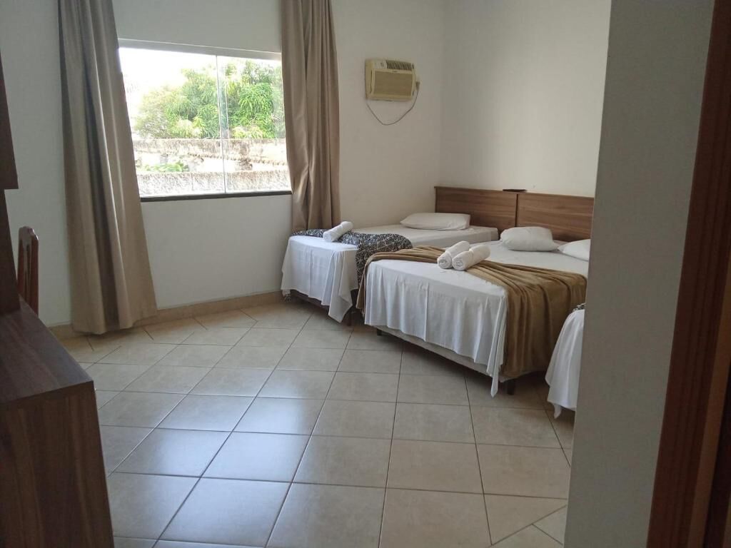 A hotel room with two beds, a window with curtains, a wooden headboard, and a tiled floor.